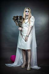 A young girl stands in a white dress with makeup for Halloween and holds a bouquet of thistles