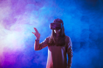 Amazed young woman touching the air during the VR experience against neon and smoke futuristic background.