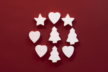 Christmas holiday concept. Abstract wreath of white stars, hearts and fir trees on burgundy background. Copy space.
