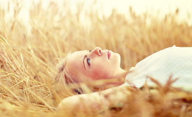 nature, summer holidays, vacation and people concept - young woman or teenage girl lying and dreaming on cereal field