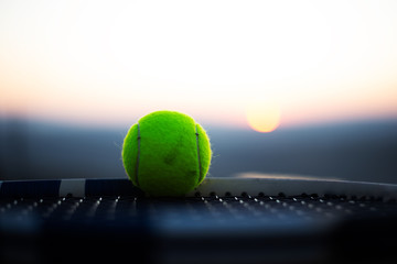Close-up of tennis ball on net of racket at sunset.