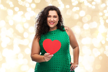 valentine's day, holidays and love concept - happy woman in green dress holding red heart over festive lights on beige background