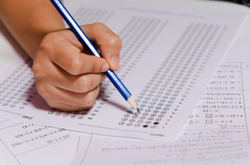 Students hand holding pencil writing selected choice on answer sheets and Mathematics question sheets. students testing doing examination. school exam