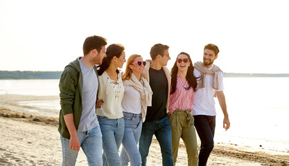 friendship, leisure and people concept - group of happy friends walking along beach in summer