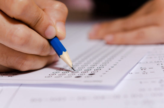 Exam. Students holding pencil writing selected choice on answer sheets and Mathematics question sheets. students testing doing examination. school exam