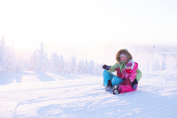 Girl and child on top of the mountain in winter clothes. The girl shows a hand in the sun, the child looks with interest. Winter landscape and sunrise, foggy haze over the forest. Winter holidays.