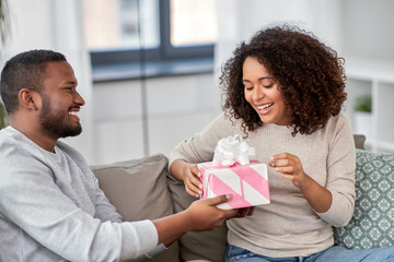 holiday, greeting and people concept - happy african american couple with gift at home