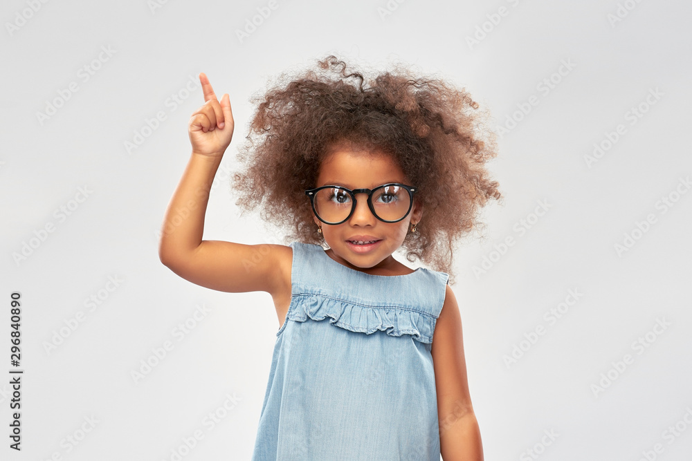 Wall mural childhood, school and education concept - happy little african american girl in glasses over grey background