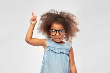 childhood, school and education concept - happy little african american girl in glasses over grey...