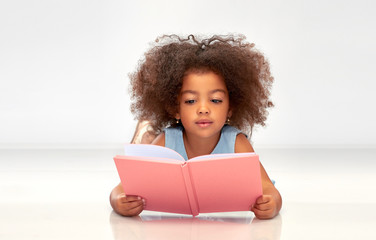 childhood, school and education concept - little african american girl reading book over grey background - obrazy, fototapety, plakaty