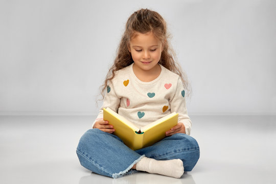 reading, education and childhood concept - beautiful smiling girl sitting on floor and reading book over grey background
