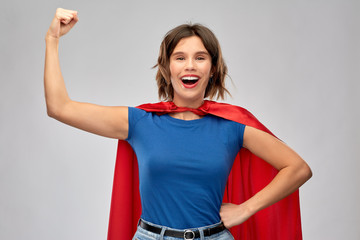 women's power and people concept - happy woman in red superhero cape showing arm bicep muscle over...
