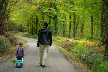 un père et son fils marchant sur une route dans les bois en automne 