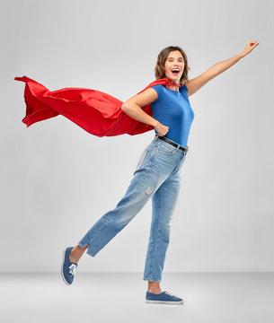 women's power and people concept - happy woman in red superhero cape making flying pose over grey background