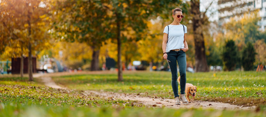Woman walking in the park with a small dog in autumn
