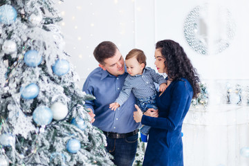 Parents and their little son near the Christmas tree. Daddy show