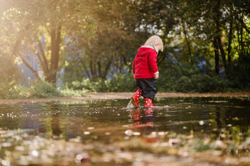 Kind mit roter Jacke und Gummistiefeln und Matschhose, Kleinkind läuft durch eine Regenpfütze 