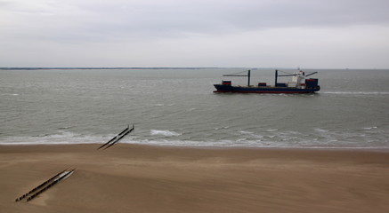 Obraz premium Panoramic view of an empty container ship passing a North Sea beach on a cloudy day in Vlissingen, Netherlands