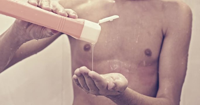 Teenager squeezes shampoo into his hand, closeup shot. 15 years old caucasian young man takes a shower in the bathroom. Slow motion.