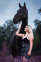 Junge Frau lehnt sich in einer Corsage an ihr Pferd in der blühenden Heide