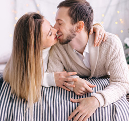 couple in white knitted sweaters lie on the bed and kiss. christ