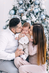 mom and dad hugging and kissing little son near christmas tree.