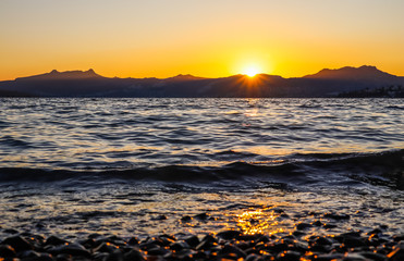 Obraz premium Beautiful sunset on the Mediterranean coast with islands and mountains. Stones on the beach lit by sunlight