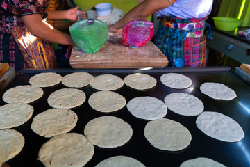 One girl makes corn tortillas and the other girl places them on the hot plate.