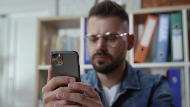 Hipster young man browsing smartphone social network in the office. In focus male hands with recent iphone modern technology device.