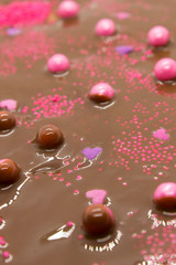 This is a photograph of Milk chocolate topped with round and heart shaped Pink and Purple sprinkles