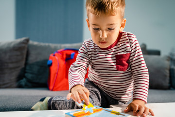 Small boy little playing at home alone by the table with puzzle developing mental skill having fun learning