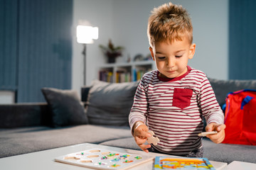 Small boy little playing at home alone by the table with puzzle developing mental skill having fun learning