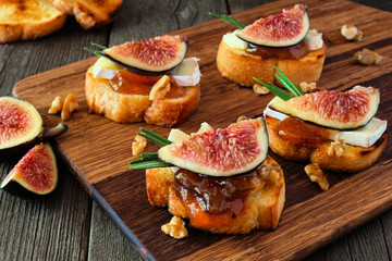 Fototapeta na wymiar Crostini appetizers with figs, brie cheese and walnuts. Close up on a wooden serving board against a dark background.