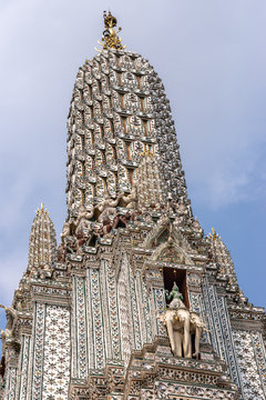 Bangkok city, Thailand - March 17, 2019: Side of Main spire or Prang of Temple of Dawn against blue sky. Porcelain and faience decoration all the way. Hindu Indra riding on Erawan statue. Shiva triden