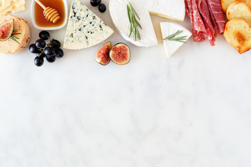 Assorted cheeses and meat appetizers. Top border, overhead view on a white marble background with...