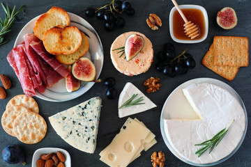 Appetizers of assorted cheeses and cured meat. Above view table scene on a dark slate background.