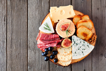 Cheese board with a selection of cheeses and meats. Top view on a rustic wooden background.