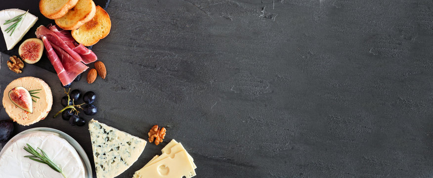 Appetizer selection of cheeses and meats. Corner border banner, above view on a slate stone background with copy space.