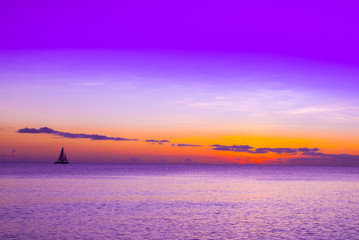 Fototapeta na wymiar A sailboat shot against the setting sun in the tropical waters of the Cayman Islands.