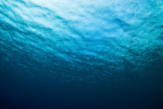 A Shot Taken From Beneath The Surface Of The Sea Looking Up At The Sky. The Light Patch Is The Sun Overhead And Through The Surface It Is Possible To See The Rain Falling Hard On The Water
