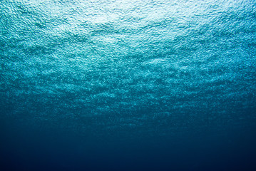 A shot taken from beneath the surface of the sea looking up at the sky. The light patch is the sun overhead and through the surface it is possible to see the rain falling hard on the water - 296863438