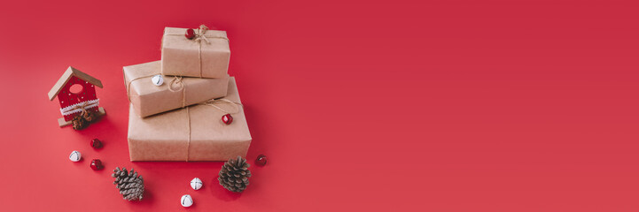 Photo of three gift boxes in kraft paper tied with ribbon. Near box lying wooden house, fir cones...