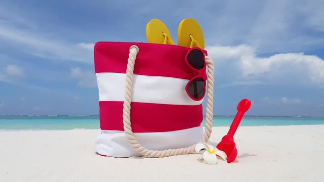 Static footage of a beach bag with hanging red sunglasses some yellow flip-flops and a red shovel with shells on its side, scenic beach in Indonesia 4K