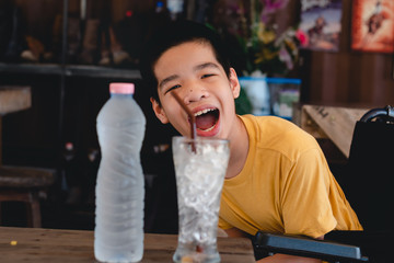 Disabled child on wheelchair eagerly looked at the cold water in the bottle,Outdoor horse farm background,Lifestyle of special child,Life in the education age of children,Happy disability kid concept.