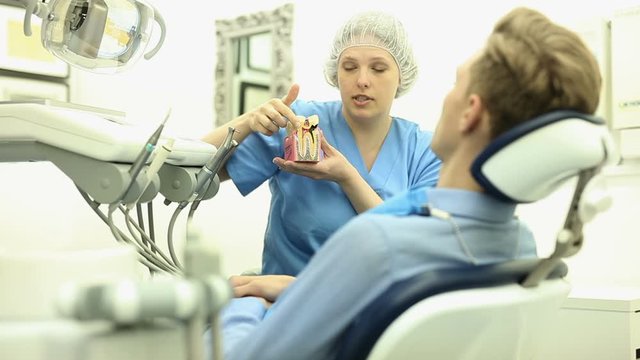 Dentist in uniform with maket of jaw is telling about healthcare in dental clinic