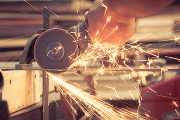 Person inside a metal smith blue collar labor workshop carefully using a metal angle grinder power...