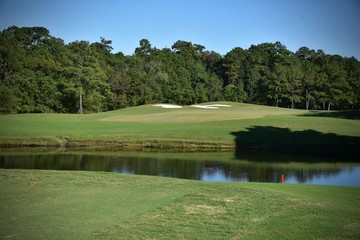 Golf course landscape, including a water hazard, sand traps and putting green on a beautiful sunny day.