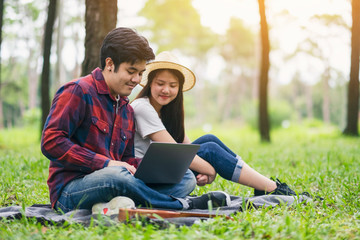 A young couple using and looking at laptop computer while sitting in the park together