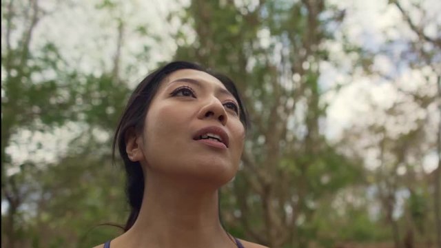 slow motion gimbal shot on young attractive tired and thirsty Asian woman drinking water after hard running workout cooling off at beautiful green park in fitness and healthy lifestyle