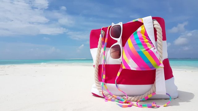 Close-up of summer bag with white and red stripes, sunglasses and swimsuit on a blur tropical background